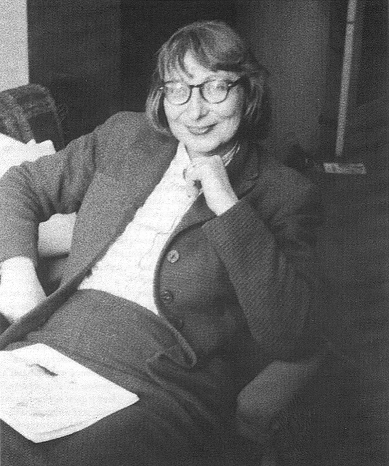 Black and white portrait of Jane Jacobs. She wears a suit, her iconic glasses, and is seated. 